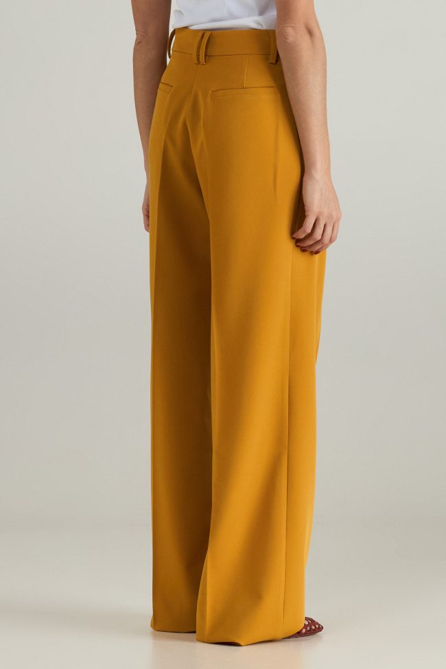Model wearing mustard yellow wide-leg trousers, styled with open sandals.