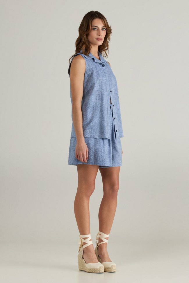 Model wearinf sleeveless light blue shirt with pointed collar and front buttons paired with matching high-waisted shorts.