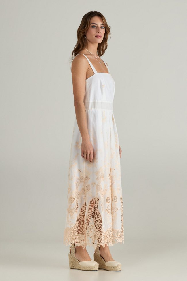 Model wearing a white sleeveless midi dress with beige broderie embroidery along the hem, wide straps and square neckline.