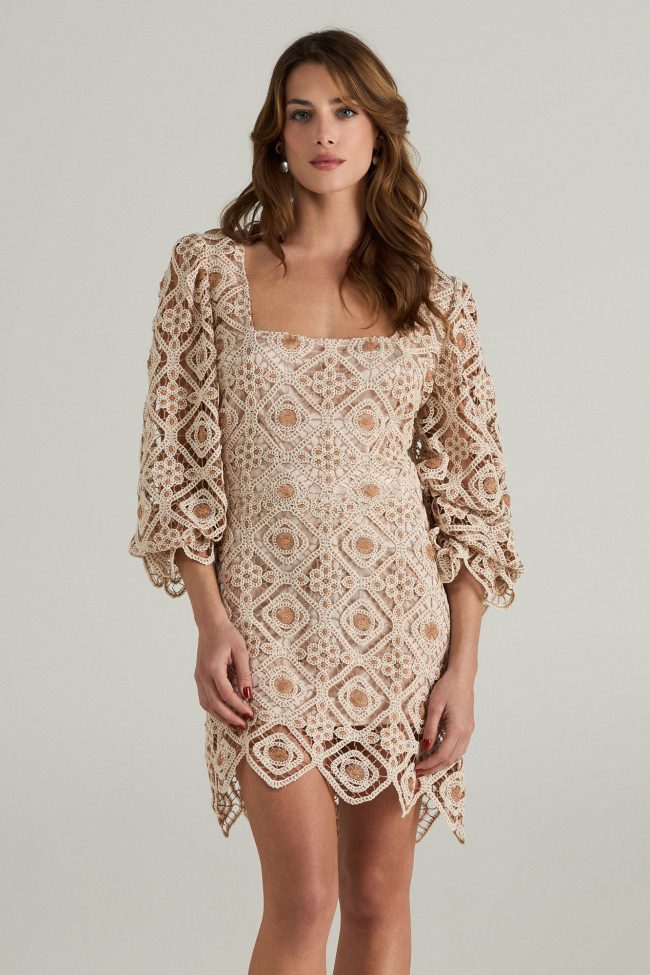 Model wearing a beige crochet mini dress with square neckline, balloon sleeves, and scalloped hemline.