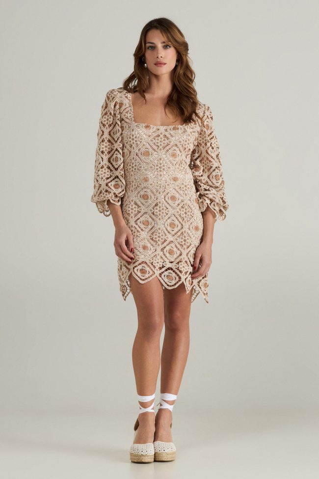 Model wearing a beige crochet mini dress with square neckline, balloon sleeves, and scalloped hemline.