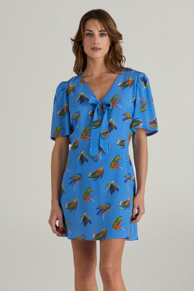 Model wearing blue mini dress with colourful insect print, puff sleeves and a bow tie neckline.