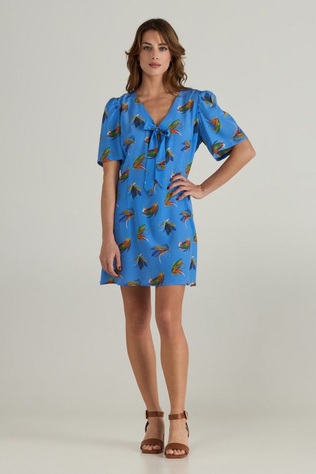 Model wearing blue mini dress with colourful insect print, puff sleeves and a bow tie neckline.