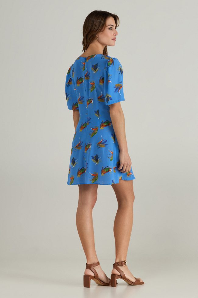 Model wearing blue mini dress with colourful insect print, puff sleeves and a bow tie neckline.