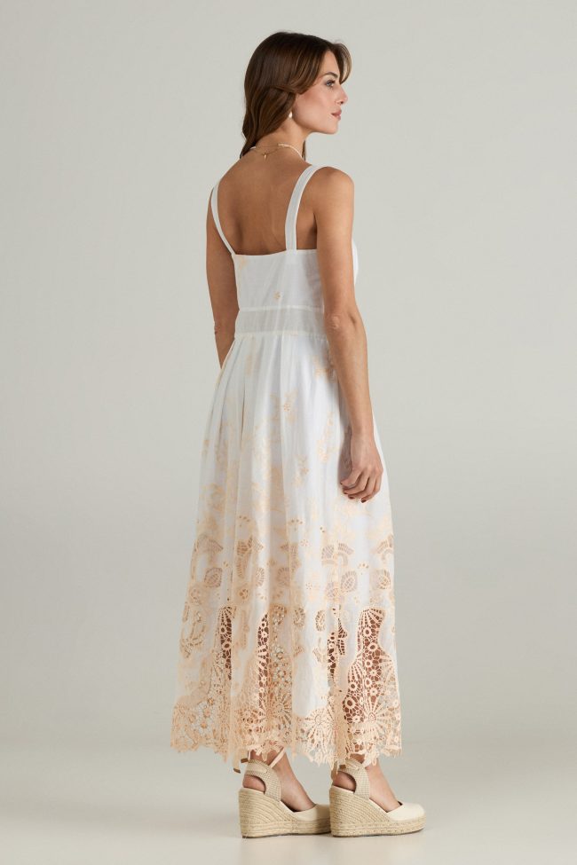 Model wearing a white sleeveless midi dress with beige broderie embroidery along the hem, wide straps and square neckline.